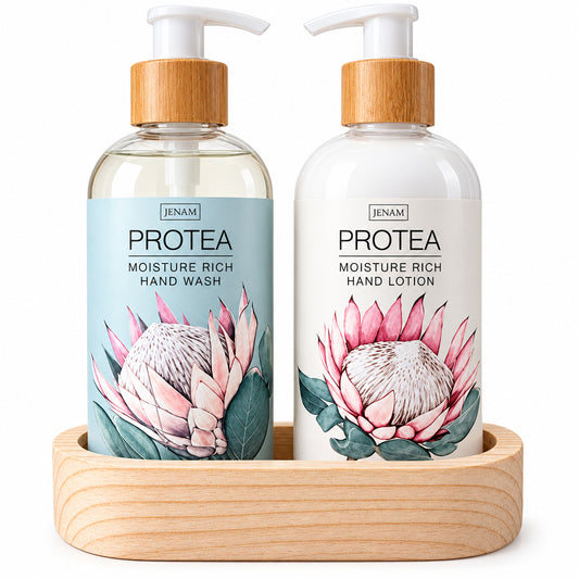 Two pump bottles from the brand JENAM, PROTEA, displayed in a light wood tray. The left bottle is a clear hand wash with a light blue label featuring a protea flower, and the right bottle is a white hand lotion with a white label featuring a pink protea flower.