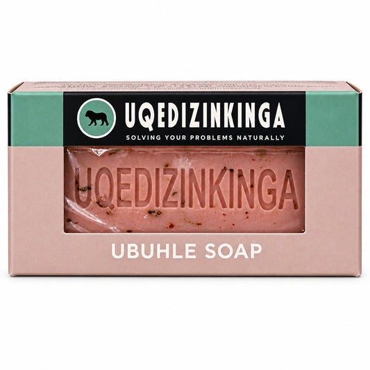 A boxed bar of Uqedizinkinga Ubuhle Soap, showing the pink soap bar through a clear window on the front of the packaging, set against a solid black background.